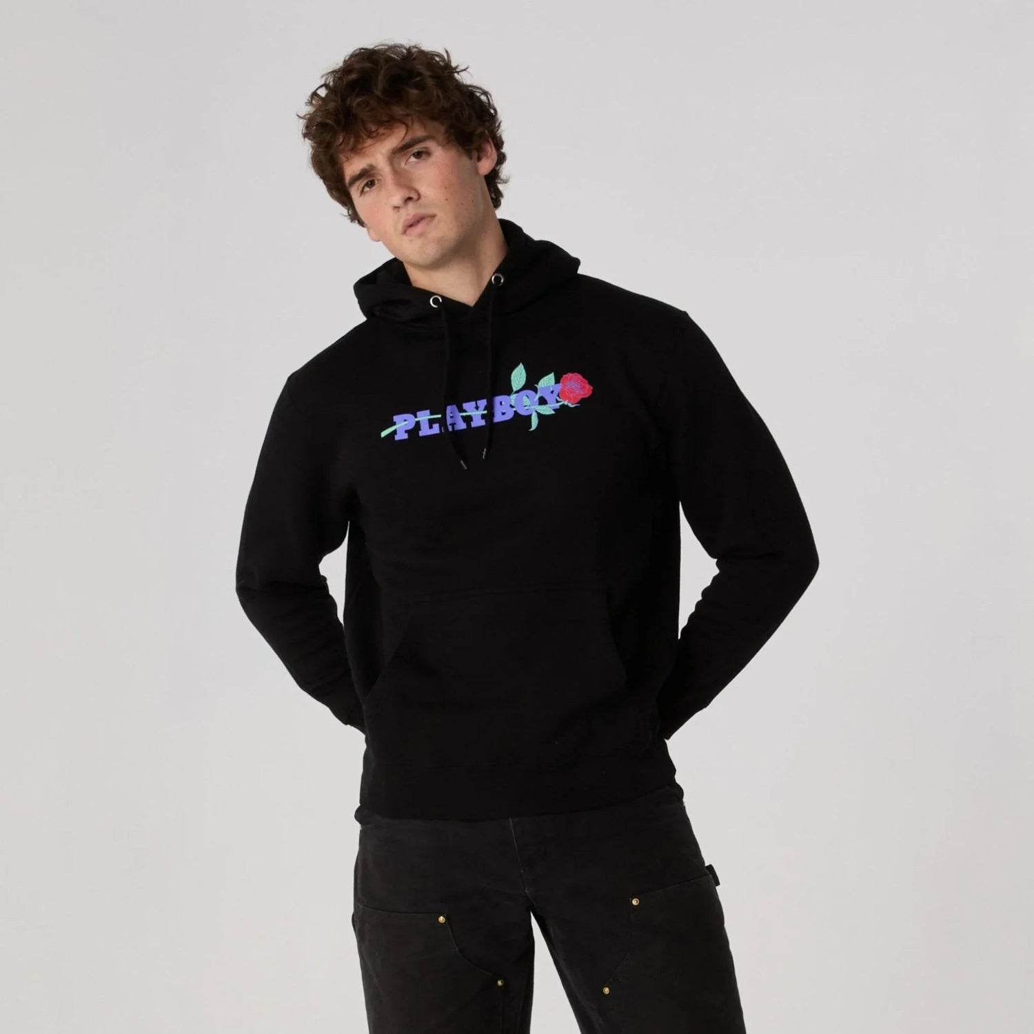 Man wearing black hoodie with colorful rose and text graphic on chest