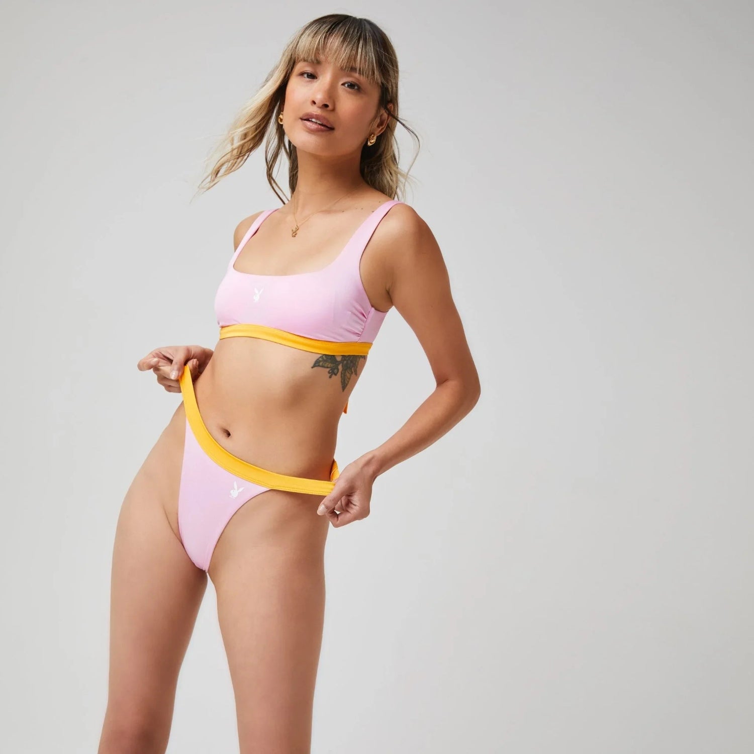 Woman modeling pink scoop bikini top and high-cut bikini bottoms with yellow trim