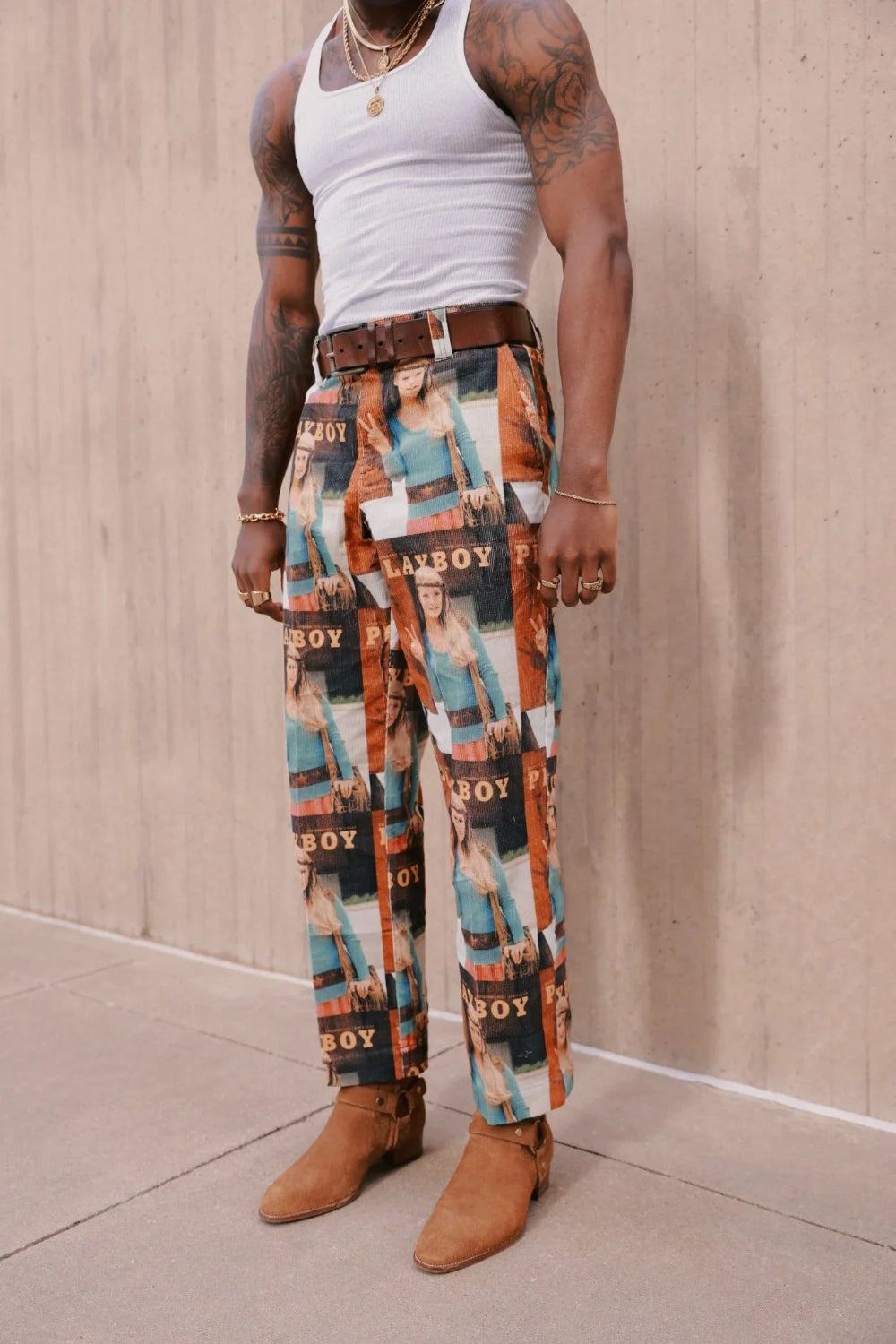 Man wearing graphic pants with vintage magazine cover print, white tank top, brown boots