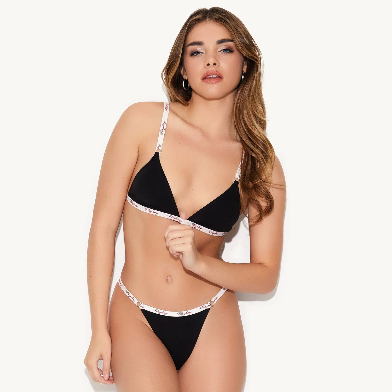 Woman modeling black triangle bralette and matching thong with logo elastic trim on white background