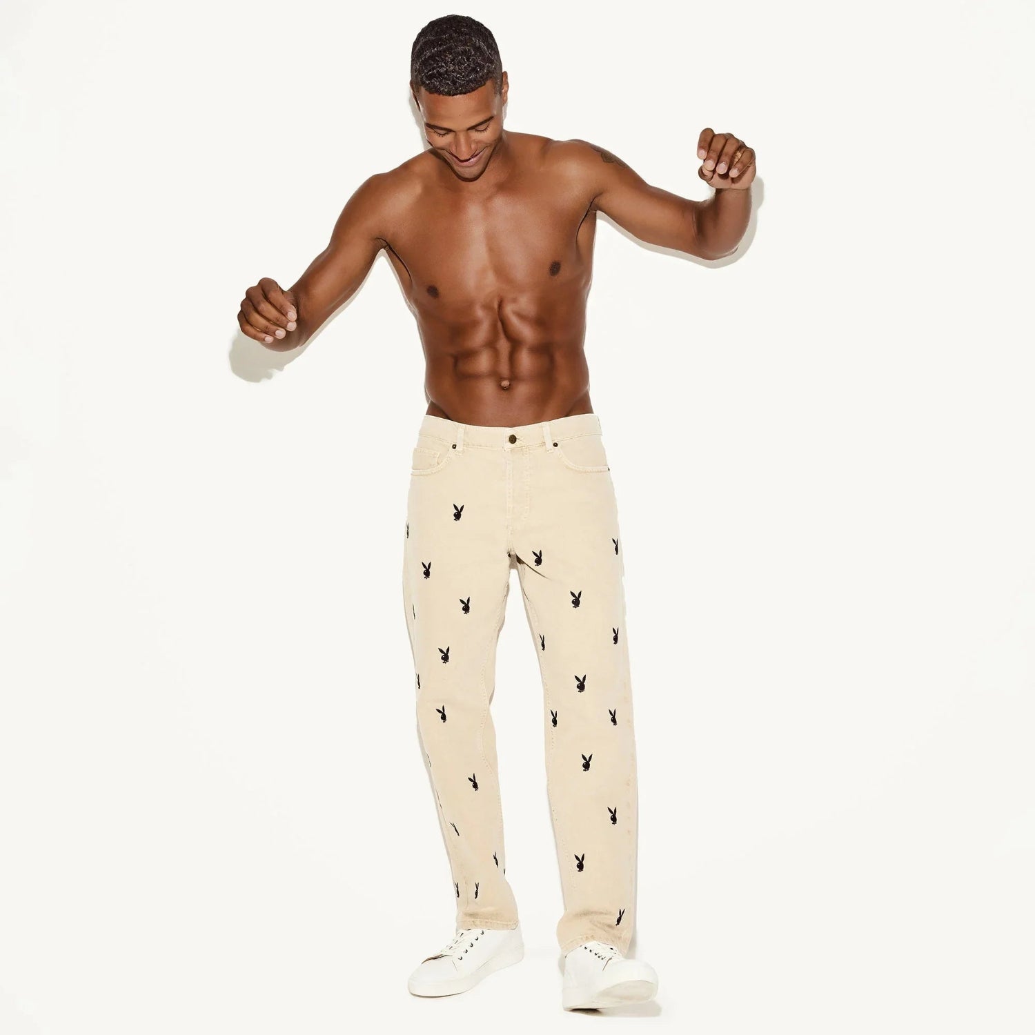 Shirtless man modeling khaki jeans with black bunny prints and white sneakers