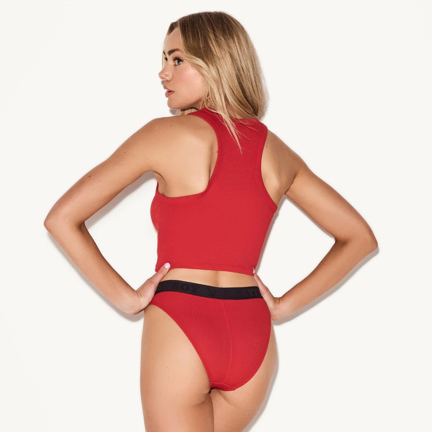 Woman wearing red ribbed tank top and high-waisted ribbed briefs, back view