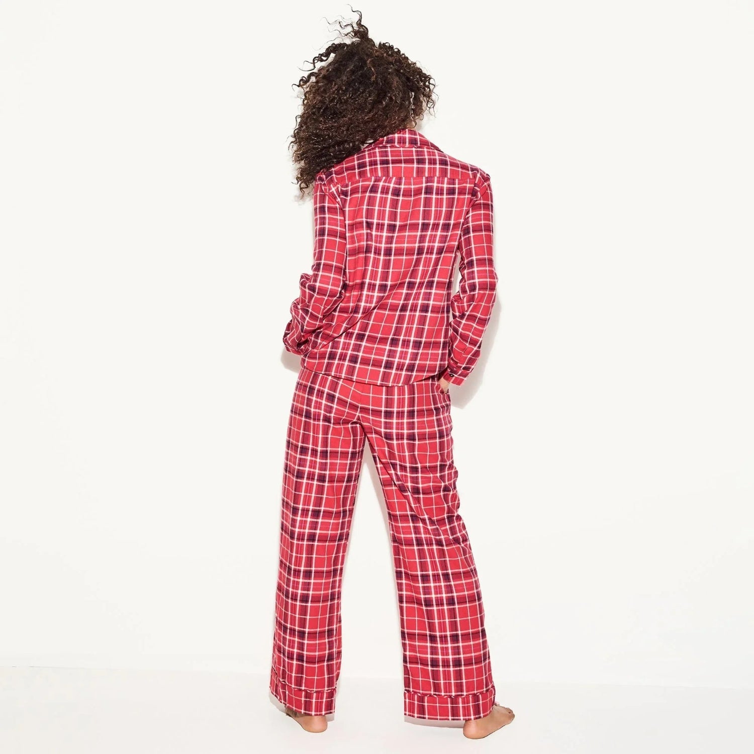 Woman wearing red plaid flannel pajama pants and matching long sleeve shirt, back view