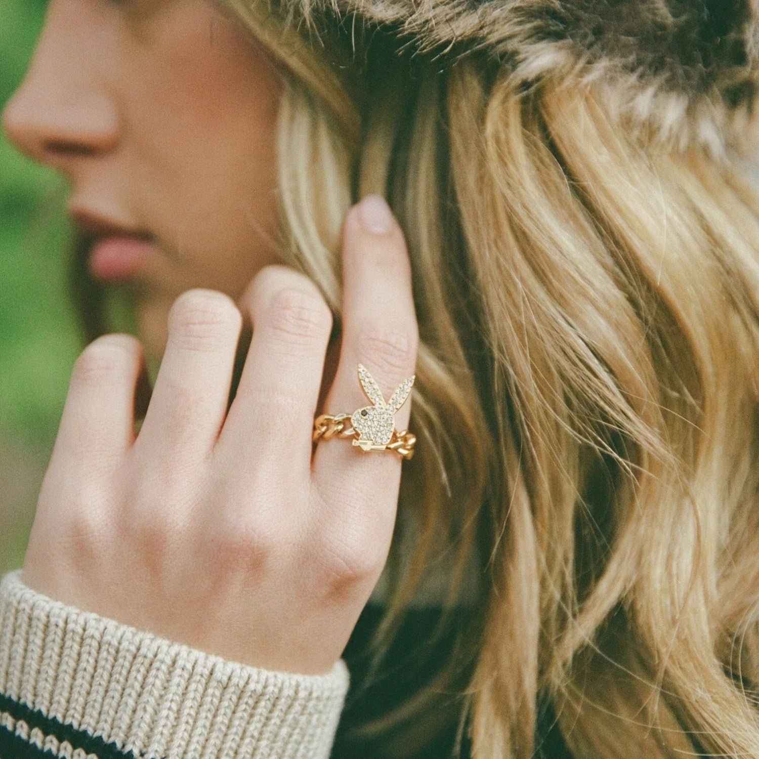 Gold bunny head chain ring worn on woman's finger with blonde hair and cozy sweater