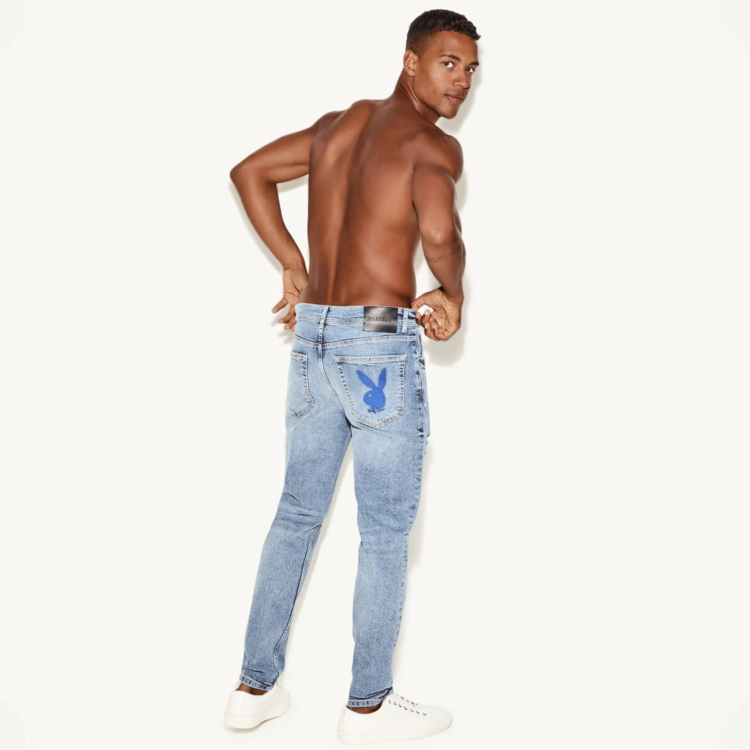 Male model in light wash skinny jeans with blue bunny graphic on back pocket, white background.
