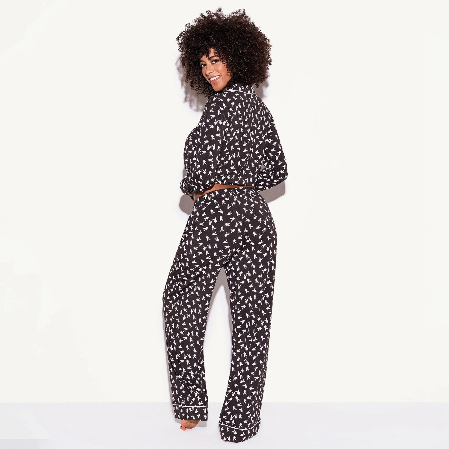 Woman modeling black pajama set with white bunny print, long sleeves and pants, on white background