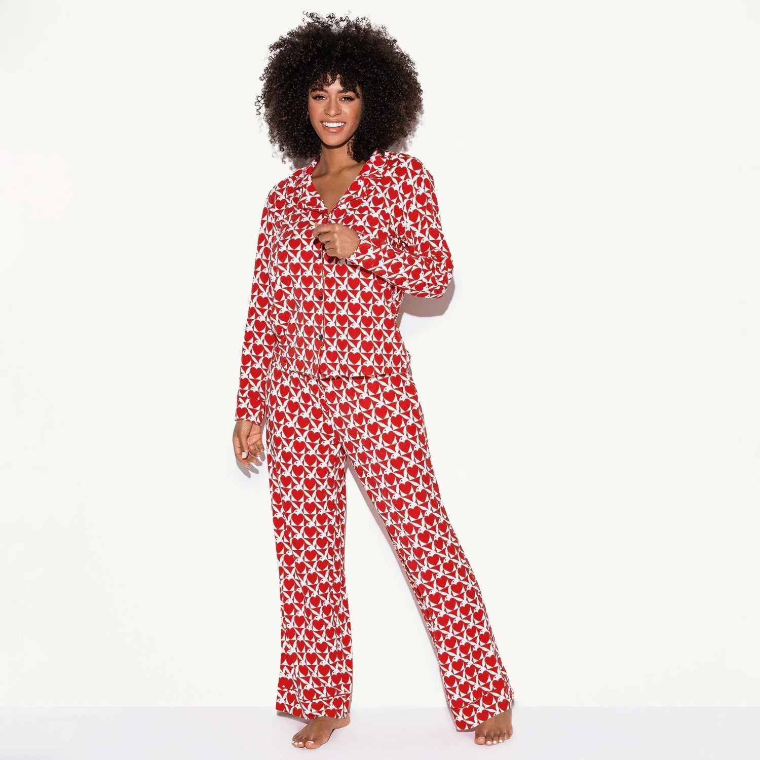 Woman wearing red and white pajama set with an all-over graphic pattern, standing barefoot.