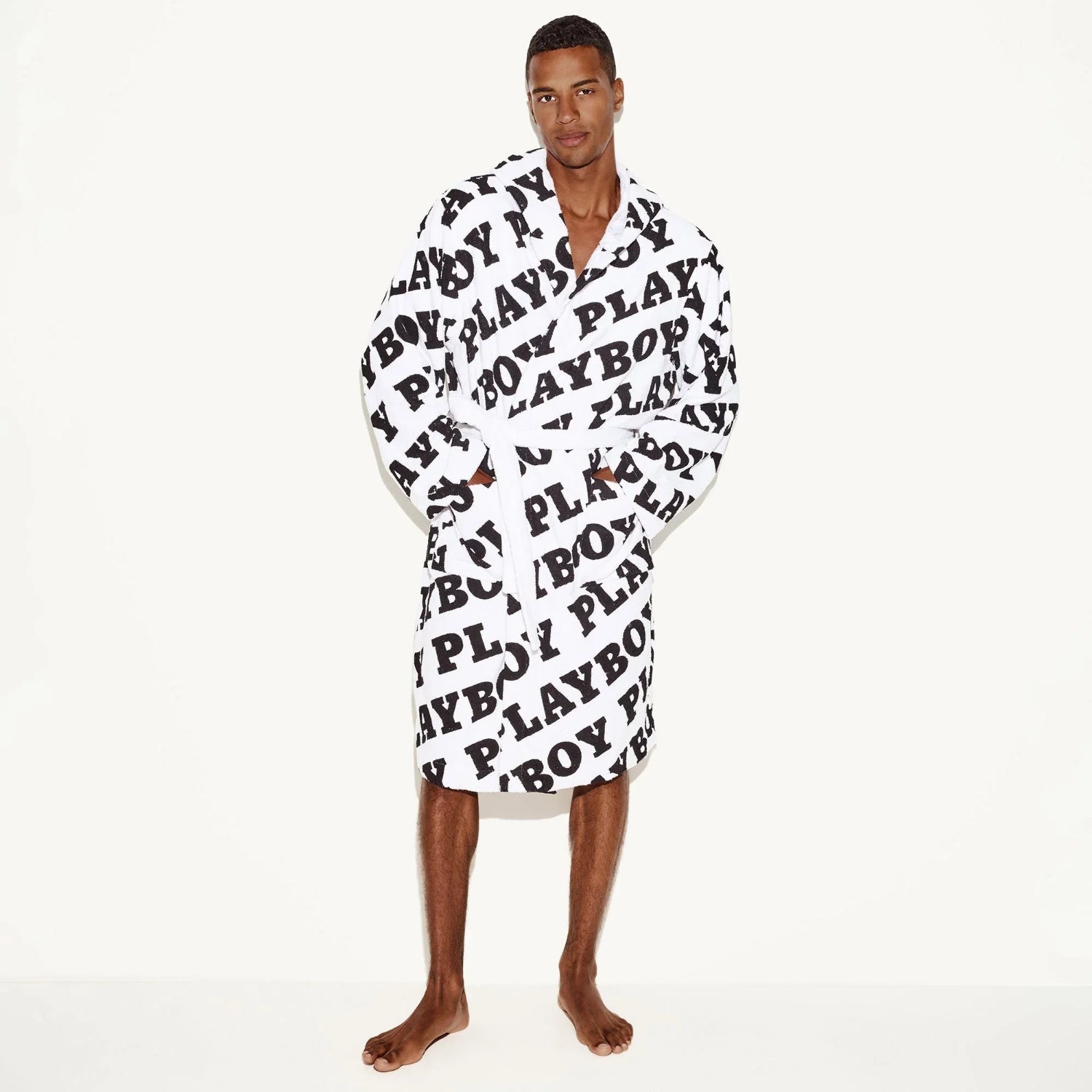 Man wearing white terry towel robe with bold black all-over text pattern, standing barefoot
