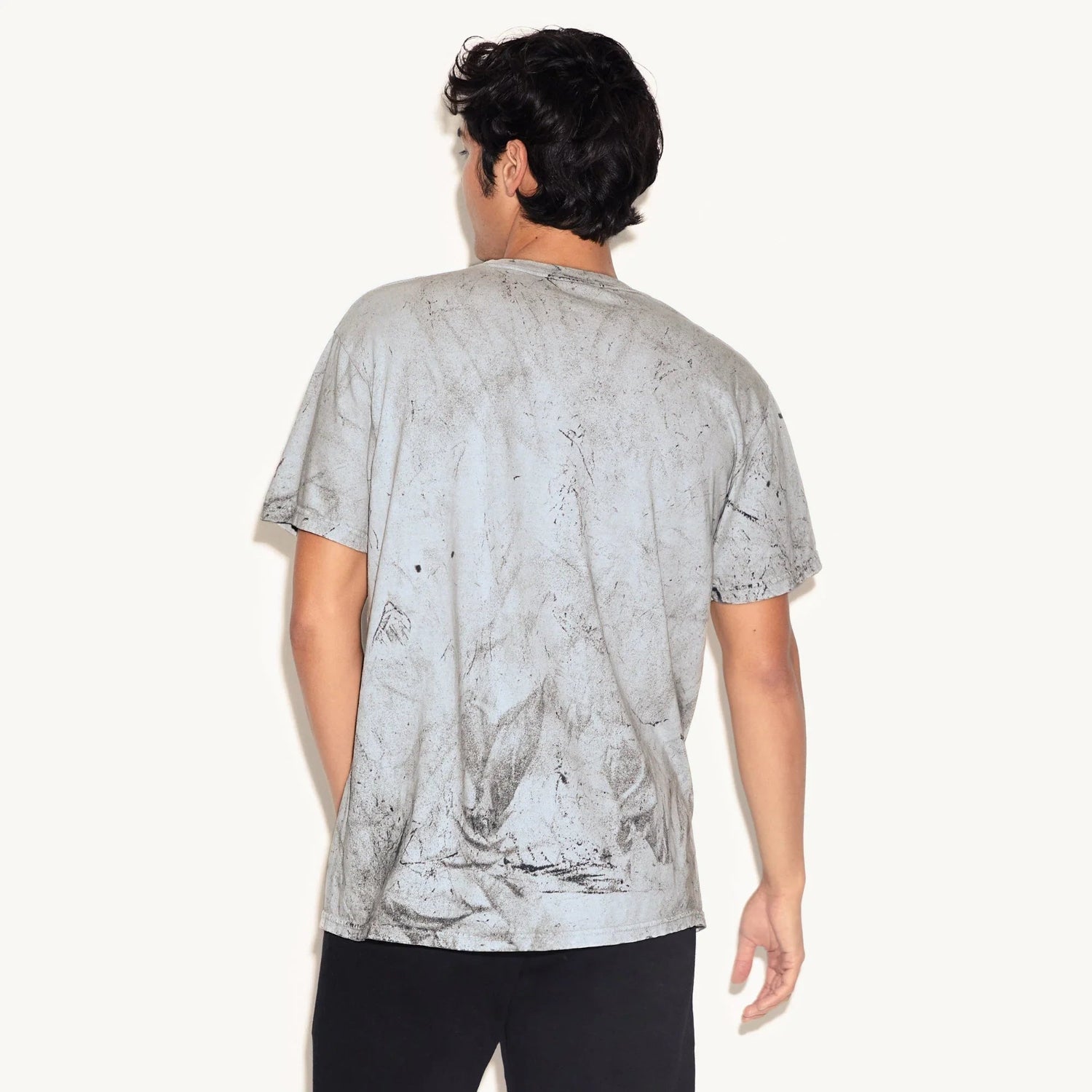 Back view of man wearing gray graphic t-shirt with faded, distressed wash and black pants