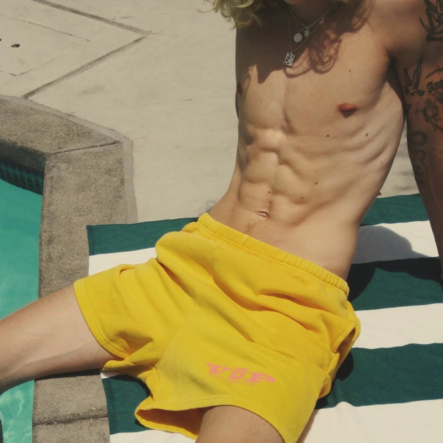 Yellow VIP Club sweat shorts on a man lounging poolside on a striped towel