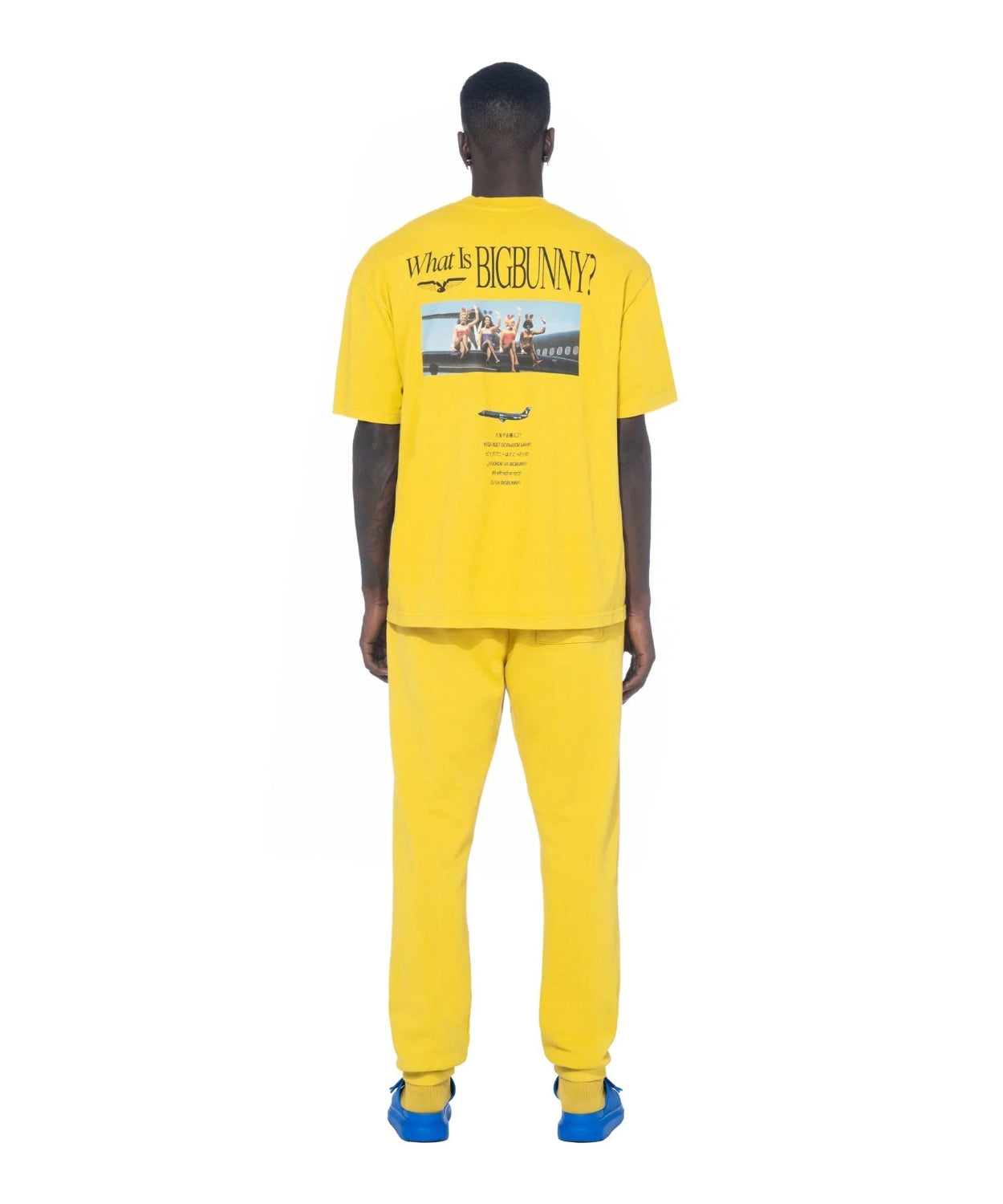 Man wearing yellow graphic t-shirt with 'What Is BigBunny?' text and plane photo on back