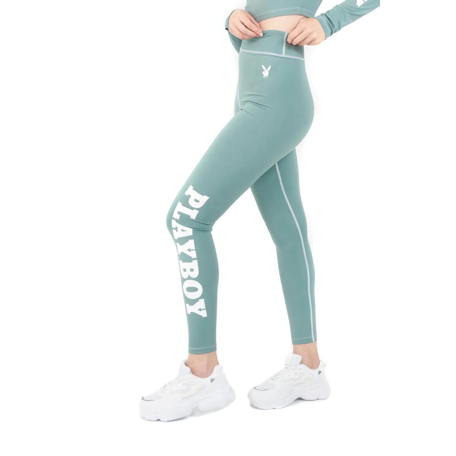 Woman wearing teal high-waisted active leggings with bold white PLAYBOY logo and bunny graphic.