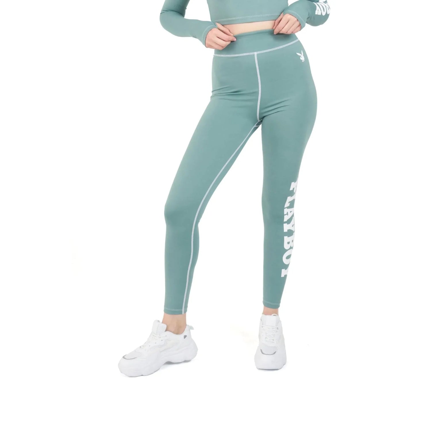 Woman wearing teal high-waisted active leggings with white side branding and white sneakers