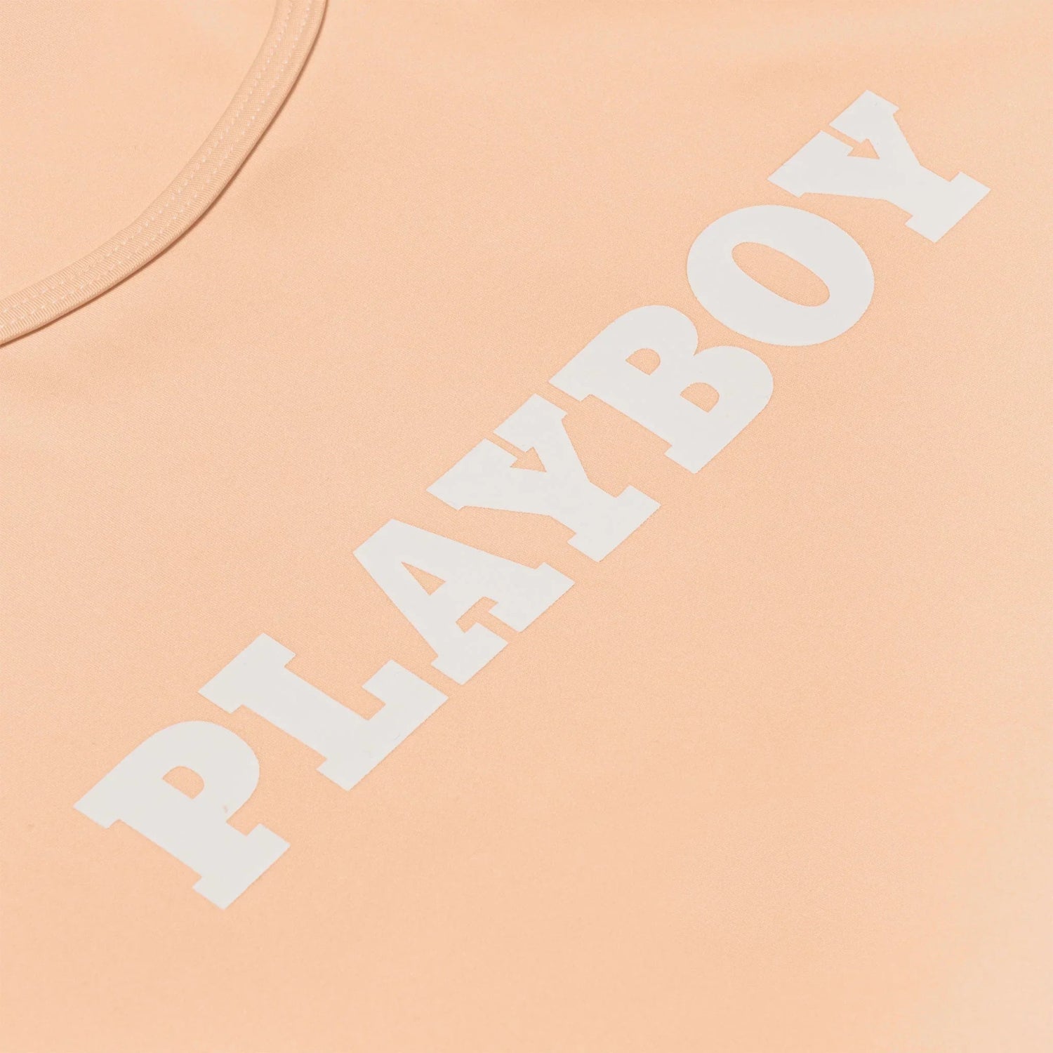 Peach women's active tee with bold white PLAYBOY logo on chest, close-up view