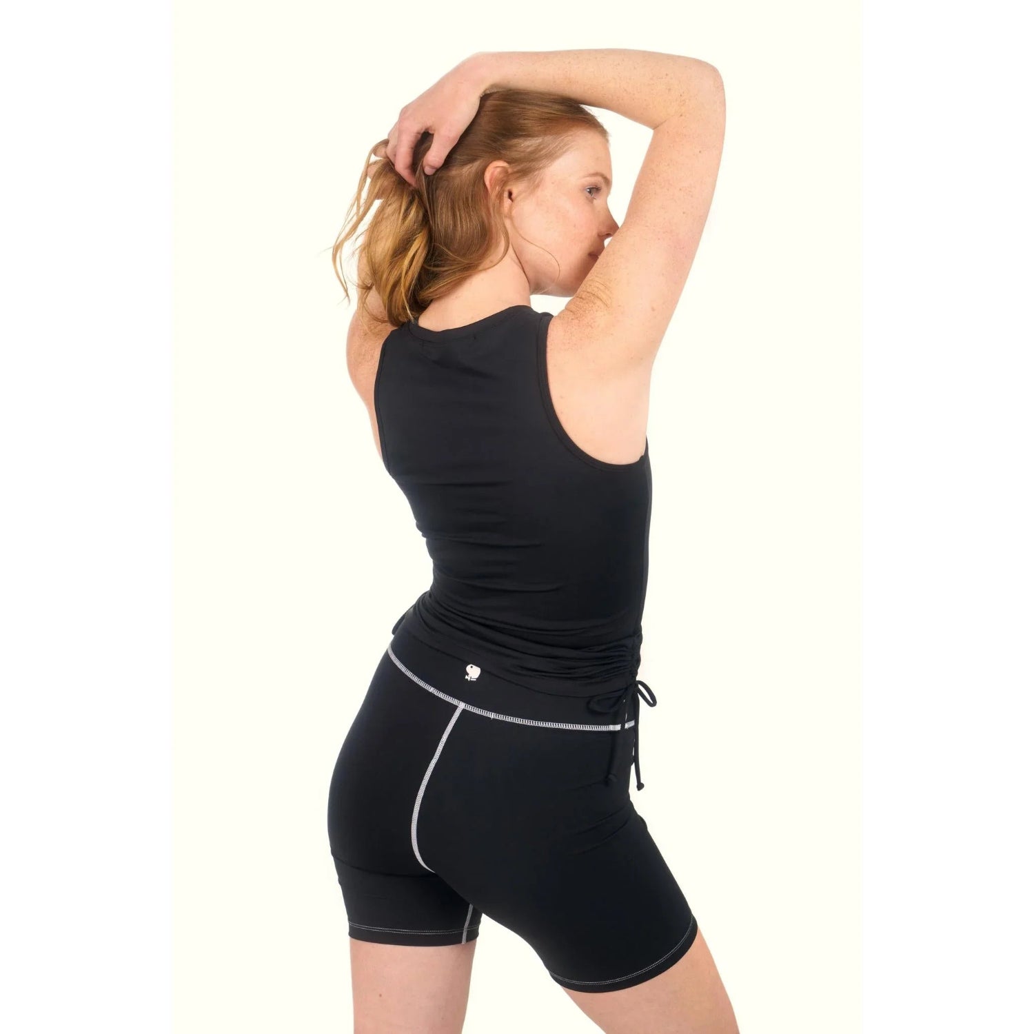 Woman wearing black ruched active tank top and matching athletic shorts, viewed from back