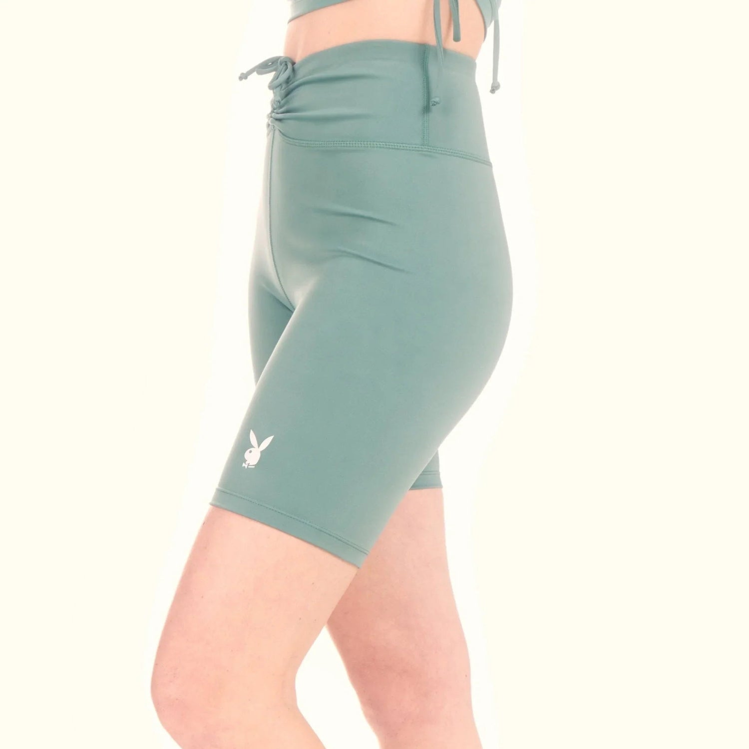 Woman wearing sage green high-waisted ruched tie bike shorts with bunny logo