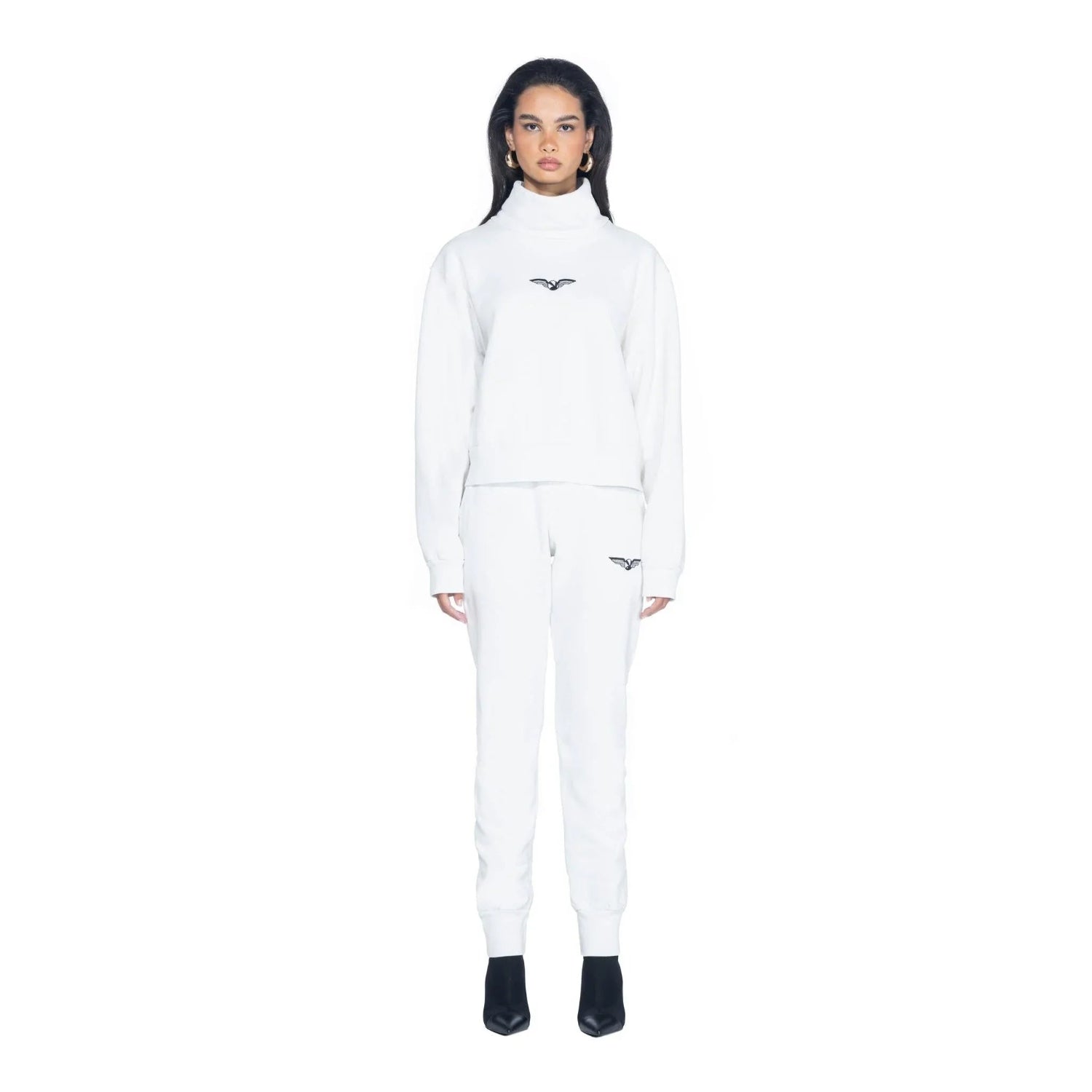 Woman wearing white high neck cropped sweatshirt and matching joggers with wing logo.