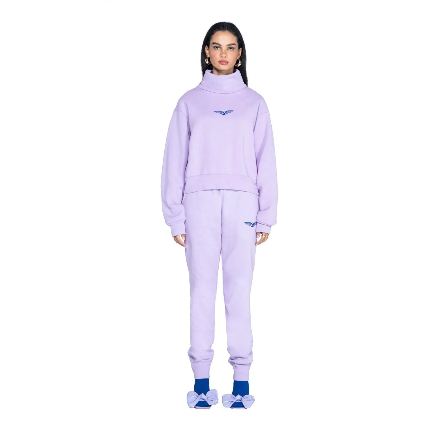 Woman wearing lavender high neck cropped sweatshirt and joggers with wing logo, blue socks, and bow slippers