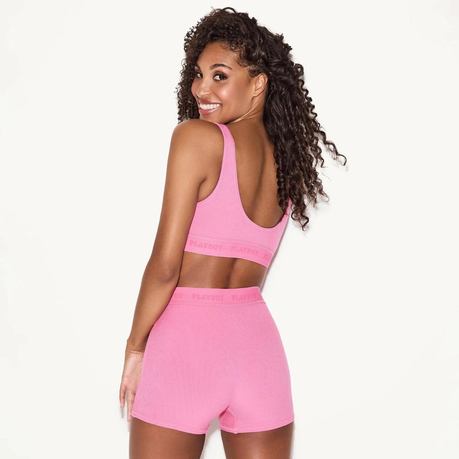 Woman wearing pink ribbed boxer brief panties and matching bralette, viewed from the back