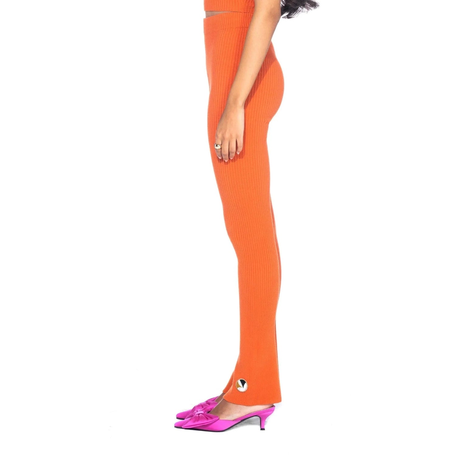 Woman wearing orange ribbed flared leggings with logo detail and pink heeled shoes