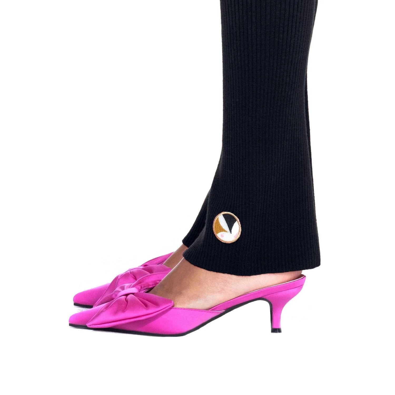 Black ribbed flared leggings with gold logo detail, styled with pink heeled mules.