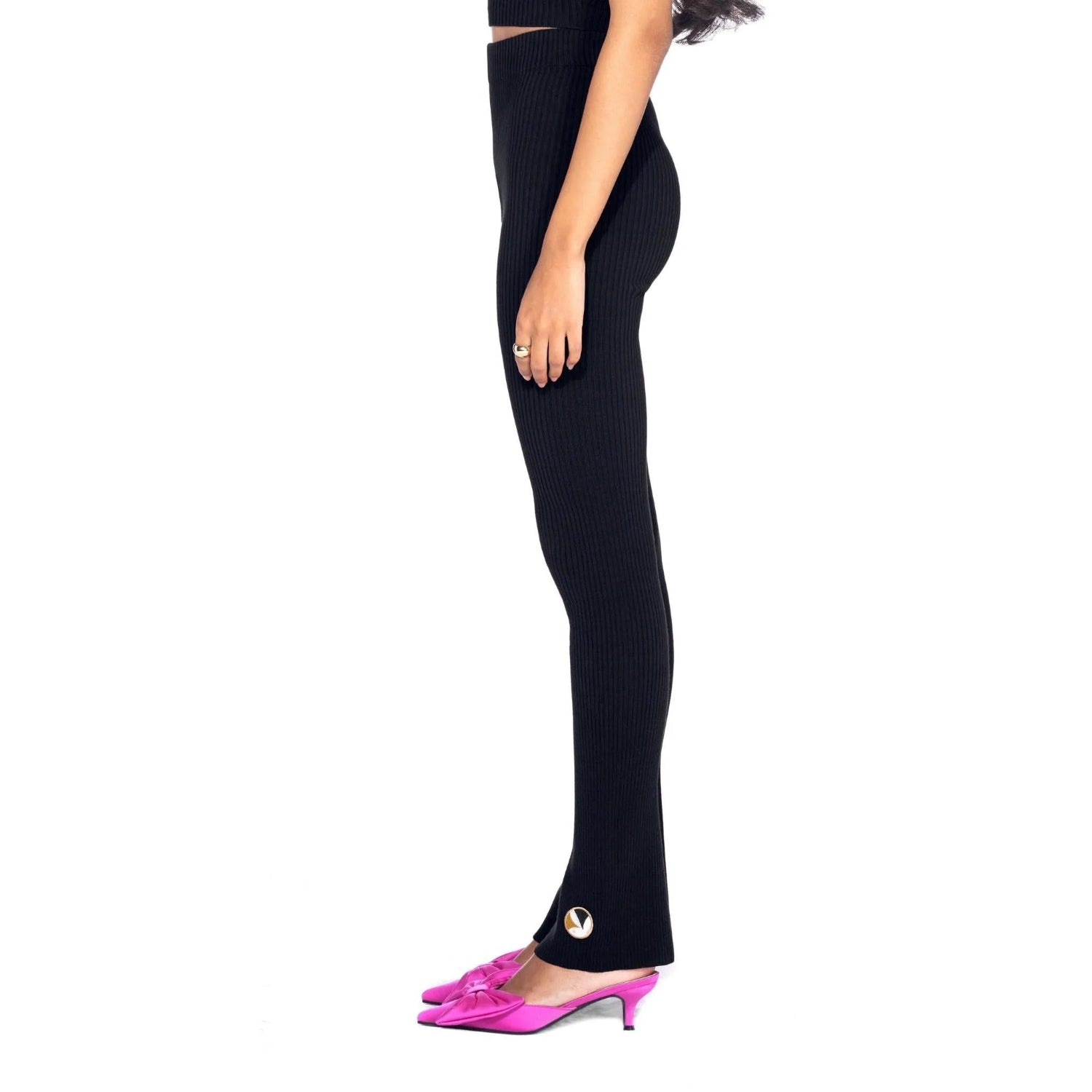 Woman wearing black flared ribbed leggings with ankle slit, pink heels, on white background