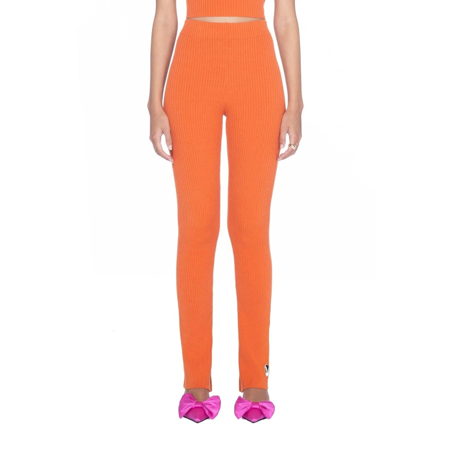 Woman wearing orange flared ribbed leggings and pink bow heels on white background