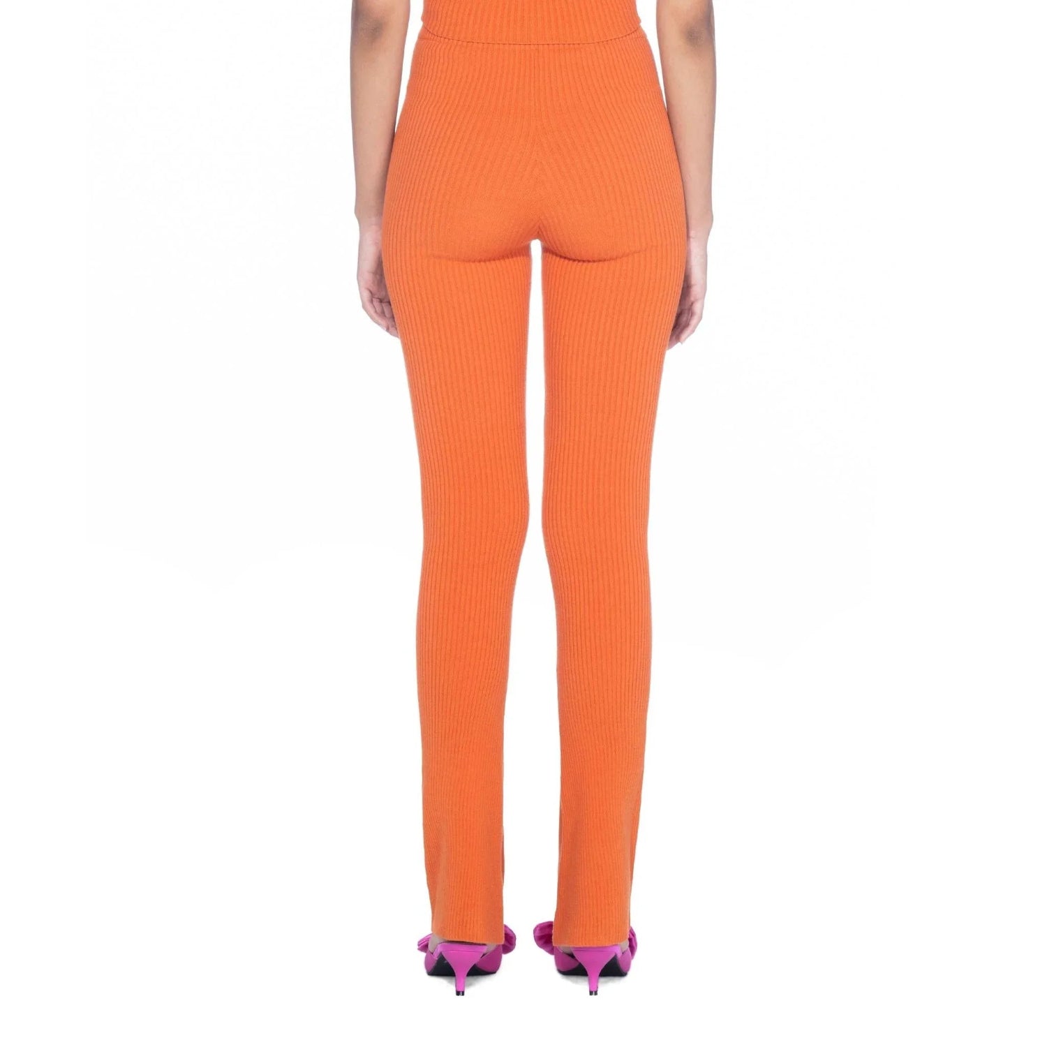 Back view of woman wearing orange flared ribbed leggings with pink heels on white background