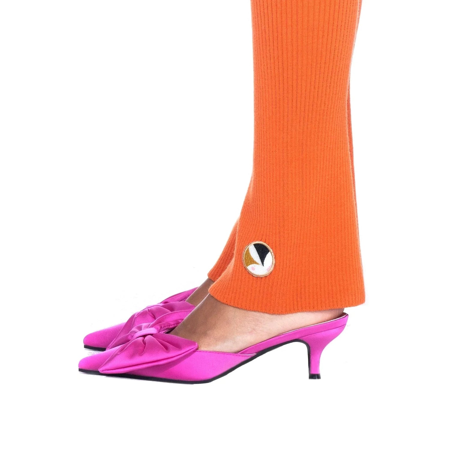 Women's orange flared ribbed leggings with side slit and logo patch, paired with pink heels