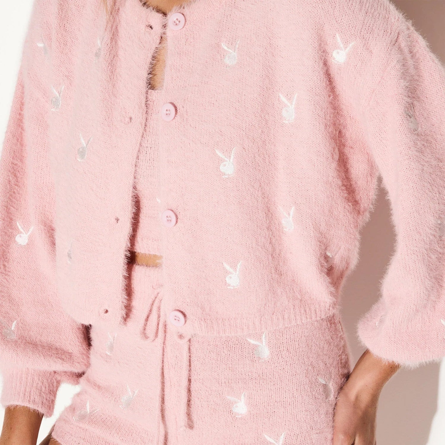 Woman wearing a pink fluffy knit crop top and cardigan with white bunny logo pattern