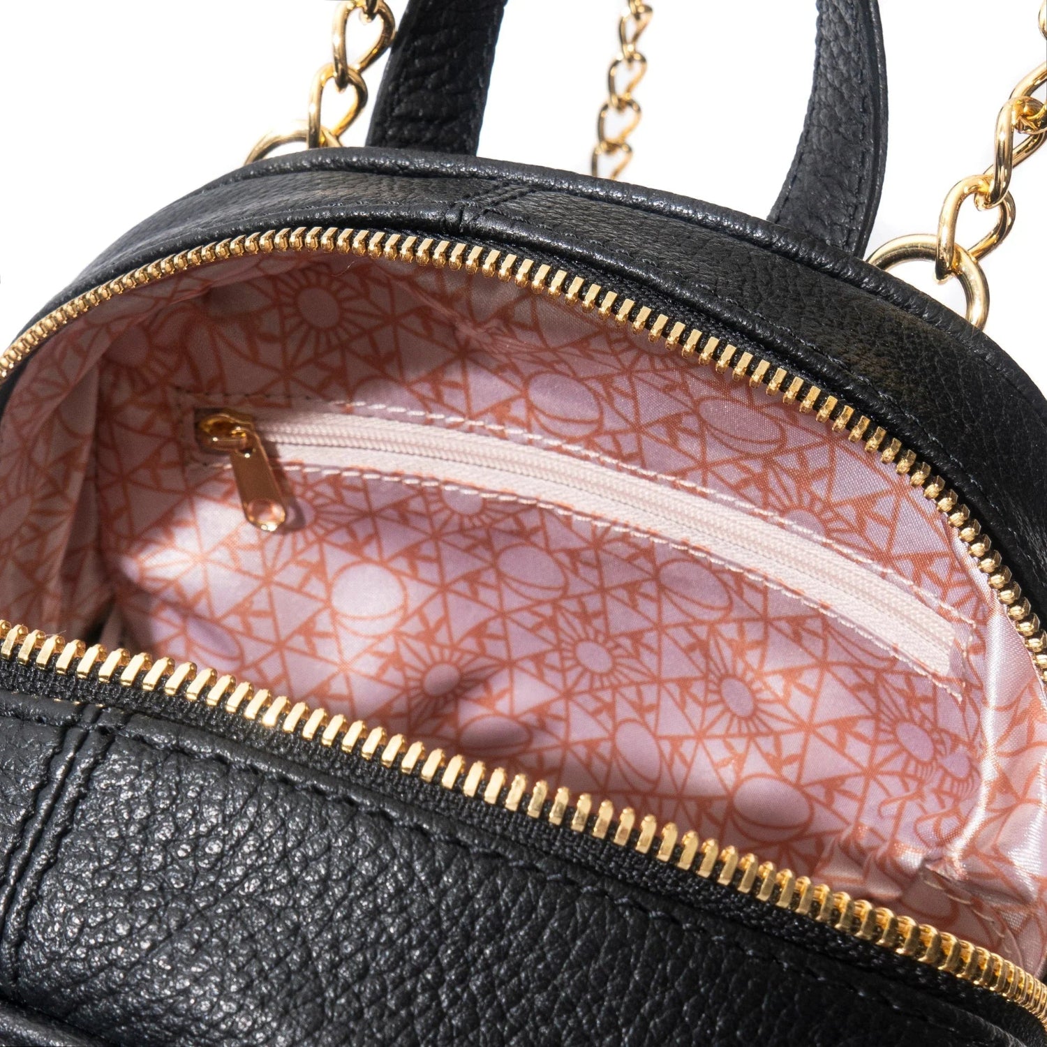 Close-up of a black leather mini backpack with gold zipper and geometric patterned pink lining.