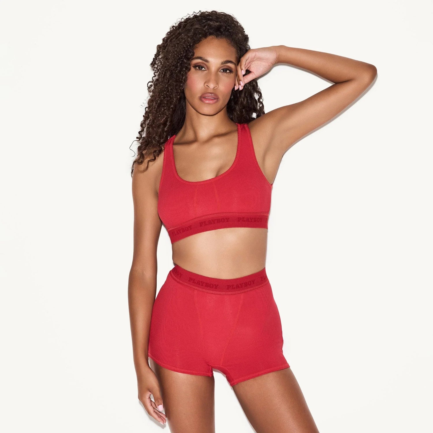 Woman modeling red sports bra and shorts set with visible logo waistband, studio background