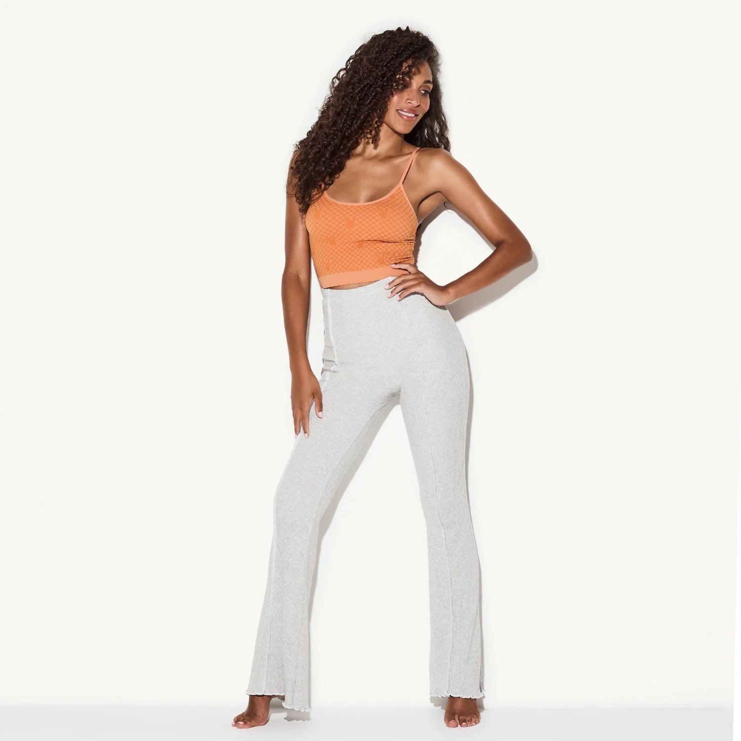 Woman modeling light gray ribbed flare pants and orange crop top on white background