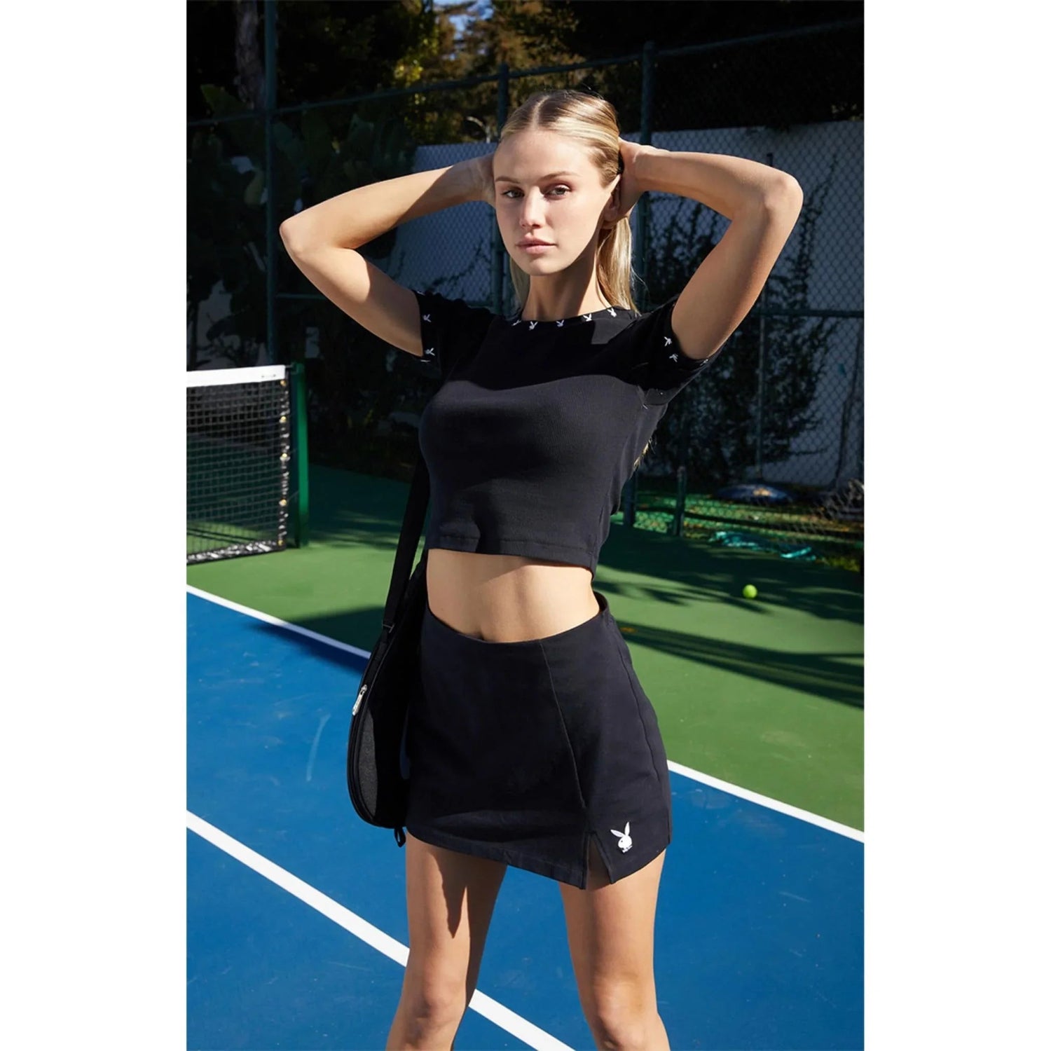 Woman on tennis court wearing black slit skirt and matching crop top with bunny logo
