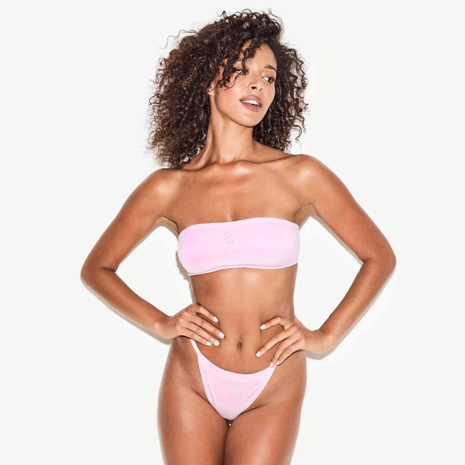 Woman wearing pink velour bandeau top and matching high-cut bottoms on white background