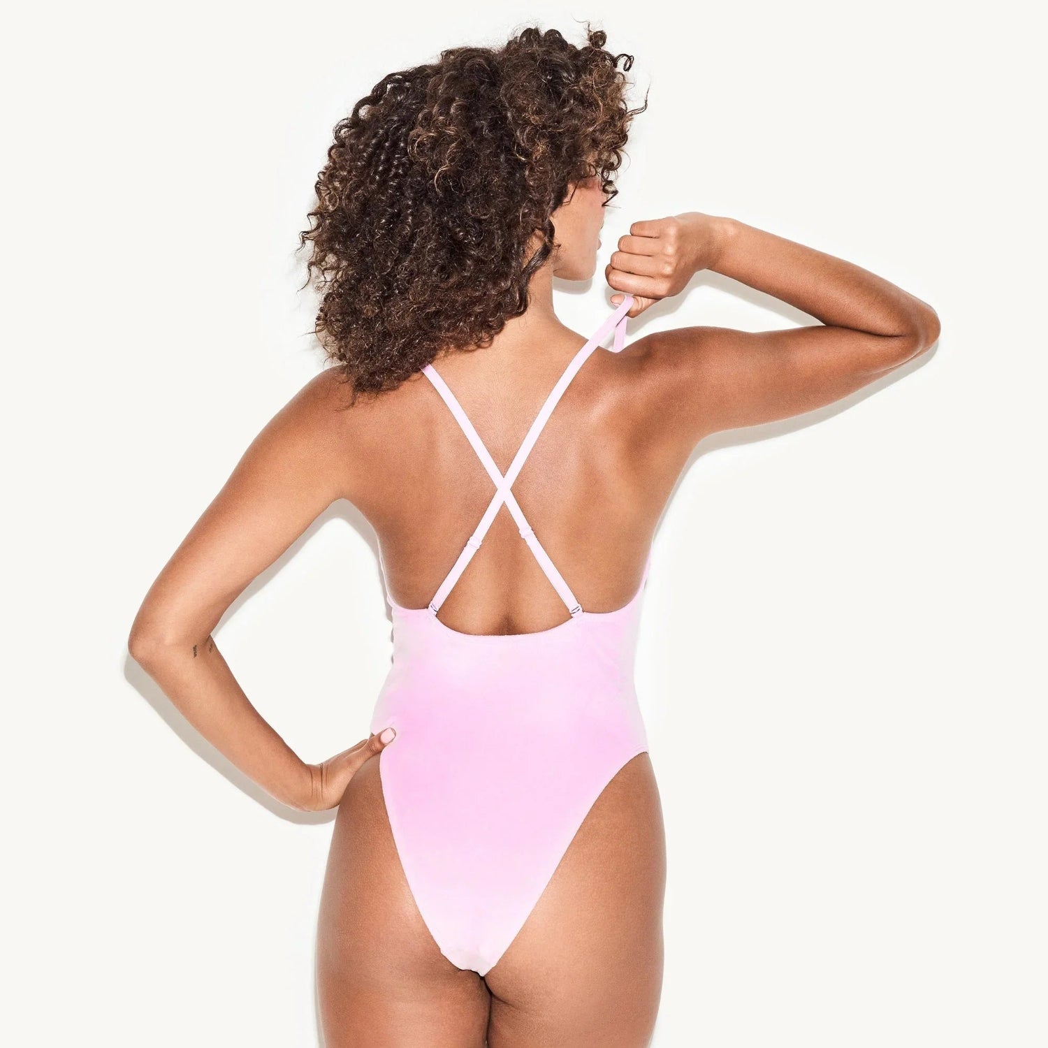Woman wearing light pink velour bodysuit with criss-cross back straps, rear view.
