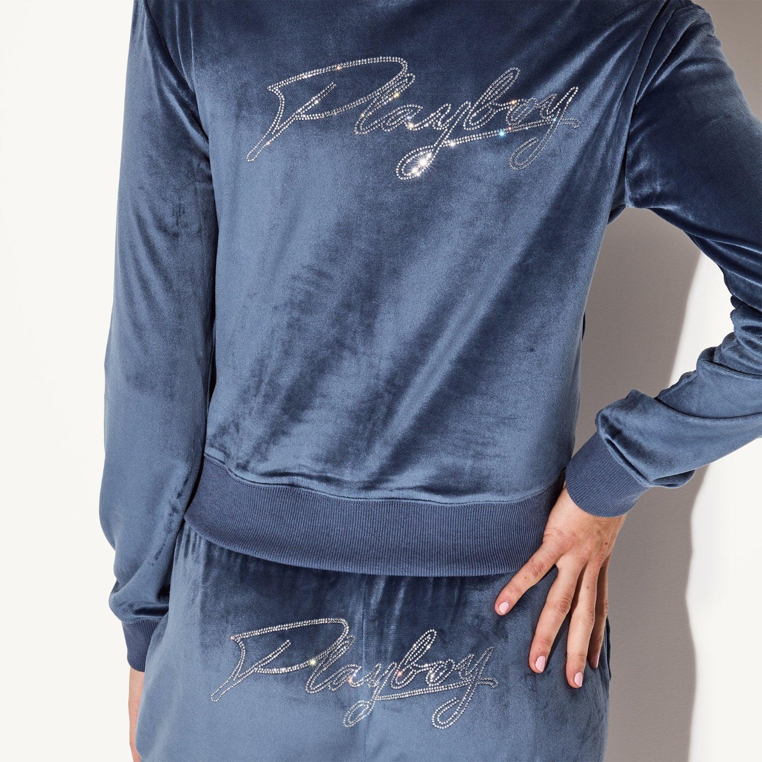 Woman wearing blue velour jacket and pants with rhinestone script logo on back