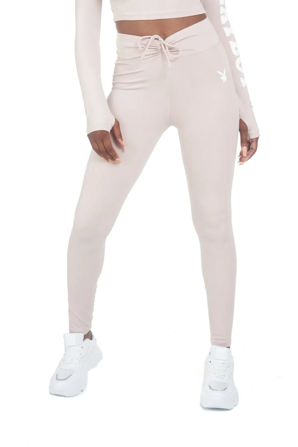 Woman wearing high-waisted beige active leggings with ruched waistband and white sneakers