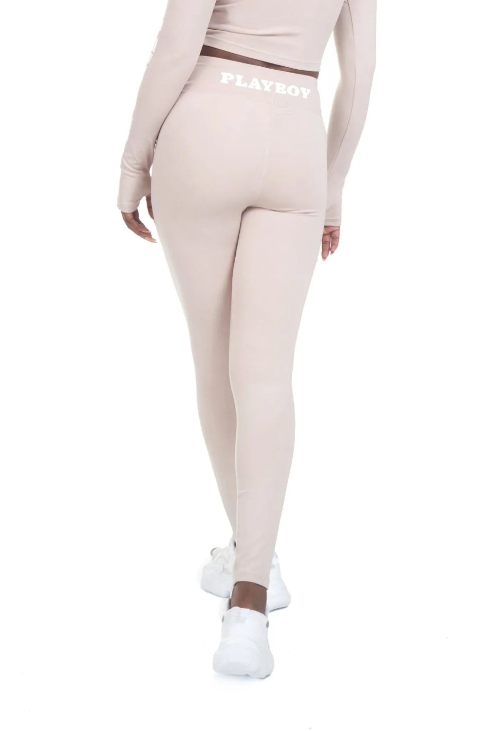 Woman wearing beige high-waisted active leggings with logo waistband, white sneakers