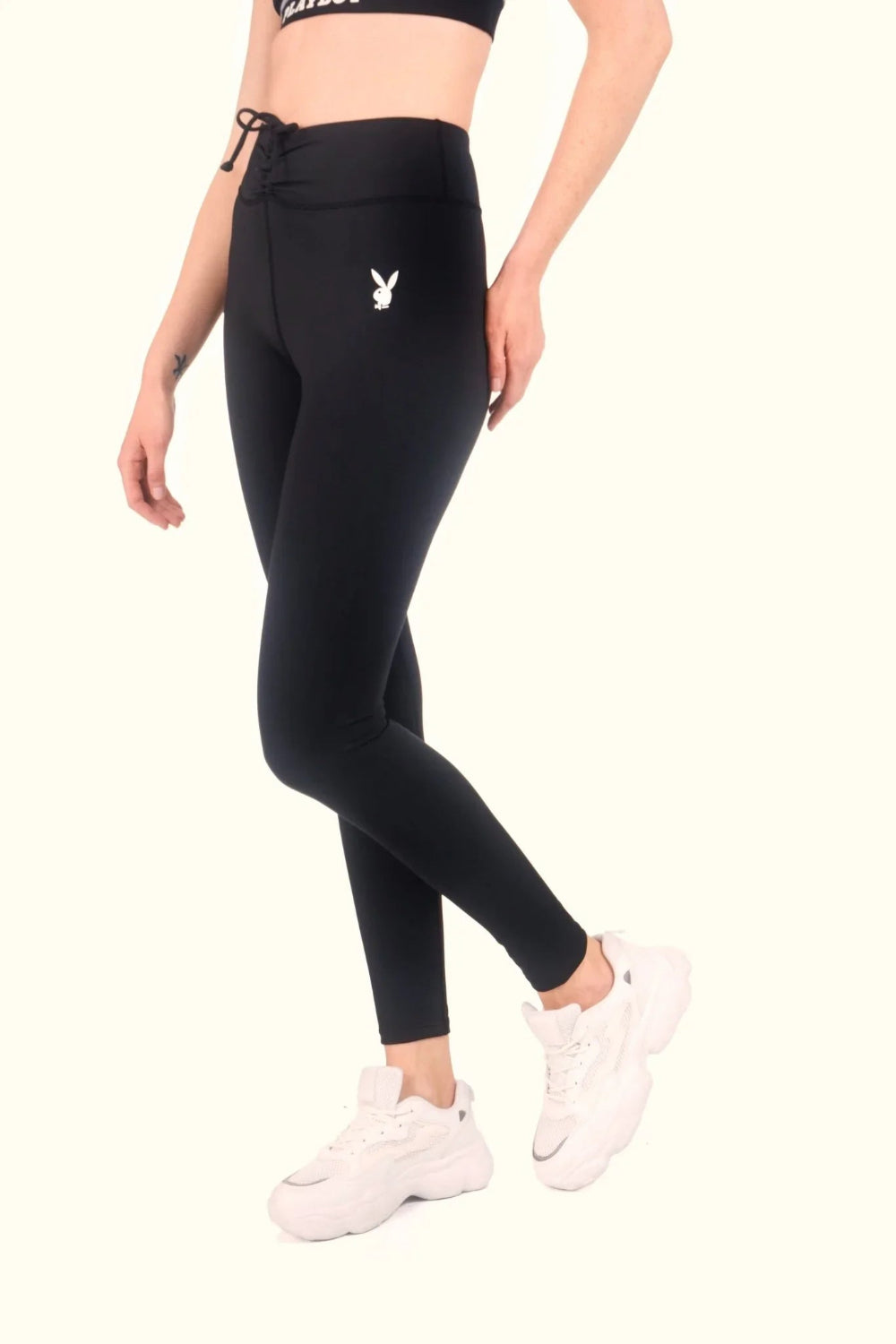 Woman wearing black ruched waistband leggings with white bunny logo and white sneakers