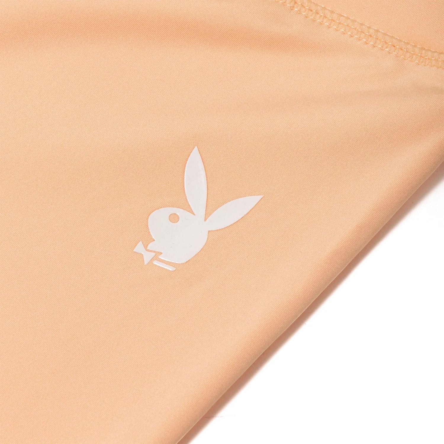 Close-up of peach active leggings with white bunny logo and ruched waistband detail